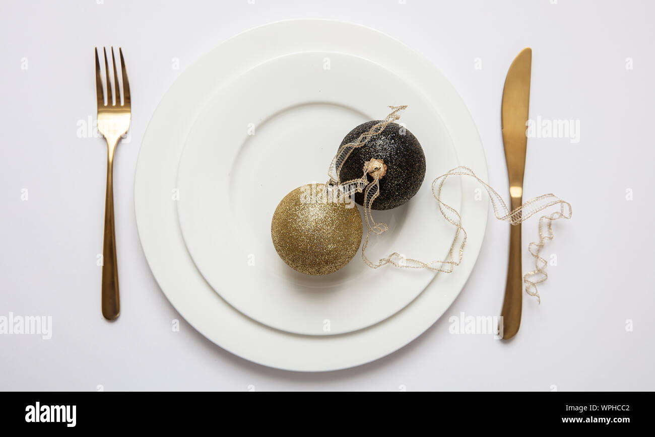 Il cenone di capodanno messa in tavola, oro xmas sfera con nastro e posate sul set di bianco di piatti, sfondo bianco, vista dall'alto Foto Stock