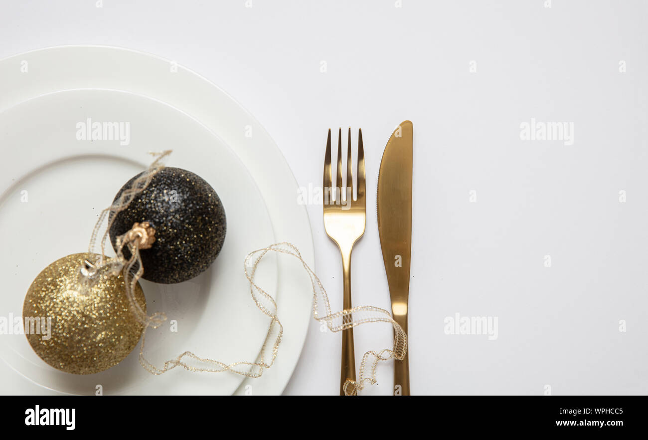 Il cenone di capodanno messa in tavola, oro xmas sfera con nastro e posate sul set di bianco di piatti, sfondo bianco, vista dall'alto Foto Stock