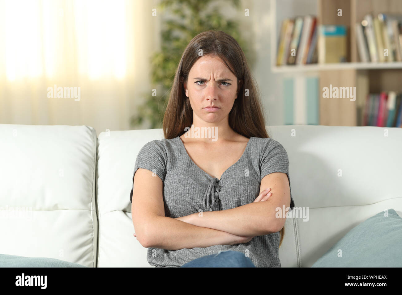 Vista frontale ritratto di una donna infastiditi guardando la telecamera seduta su un divano nel salotto di casa Foto Stock
