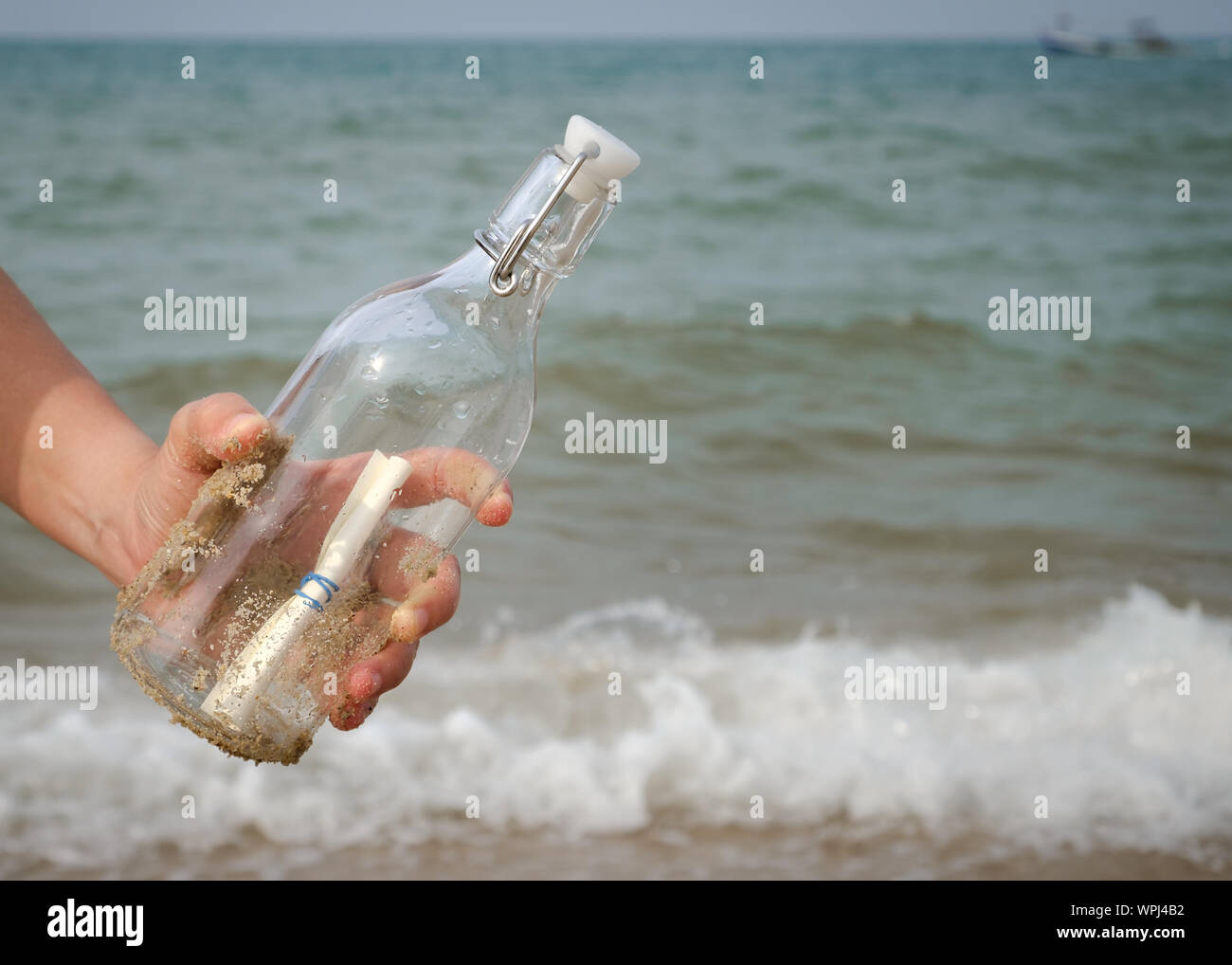 Mano che tiene una bottiglia con una lettera inserita all'interno del mare. Foto Stock