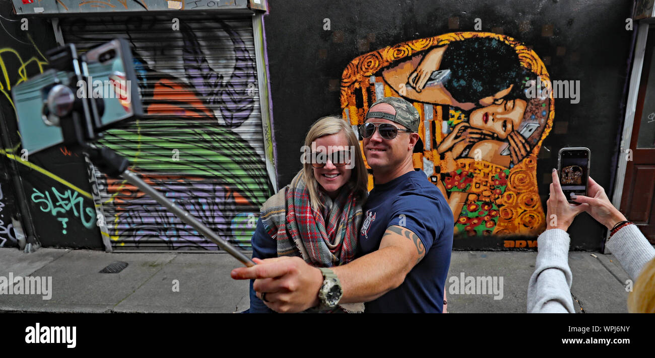 I turisti scattare una foto di arte di strada da Irish stencil ADW artista nel centro della città di Dublino. L'immagine basata su Il Bacio di Gustav Klimt mette in luce la piaga del telefono cellulare dipendenza. Foto Stock