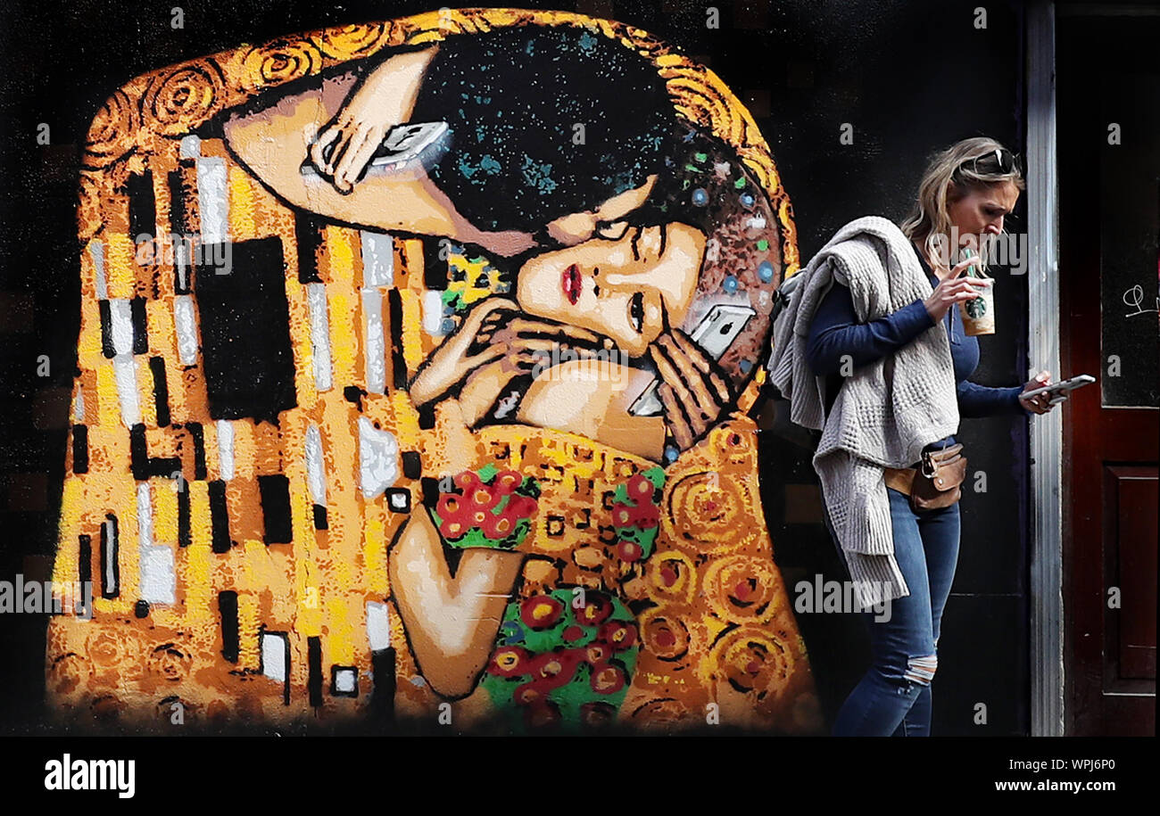 Una donna cammina passato arte di strada da Irish stencil ADW artista nel centro della città di Dublino. L'immagine basata su Il Bacio di Gustav Klimt, mette in luce la piaga del telefono cellulare dipendenza. Foto Stock