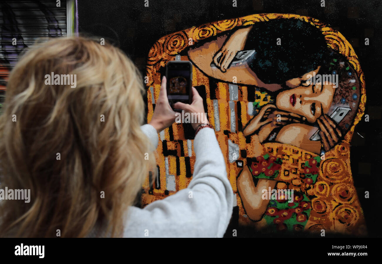 Un turista prende una foto di arte di strada da Irish stencil ADW artista nel centro della città di Dublino. L'immagine basata su Il Bacio di Gustav Klimt, mette in luce la piaga del telefono cellulare dipendenza. Foto Stock
