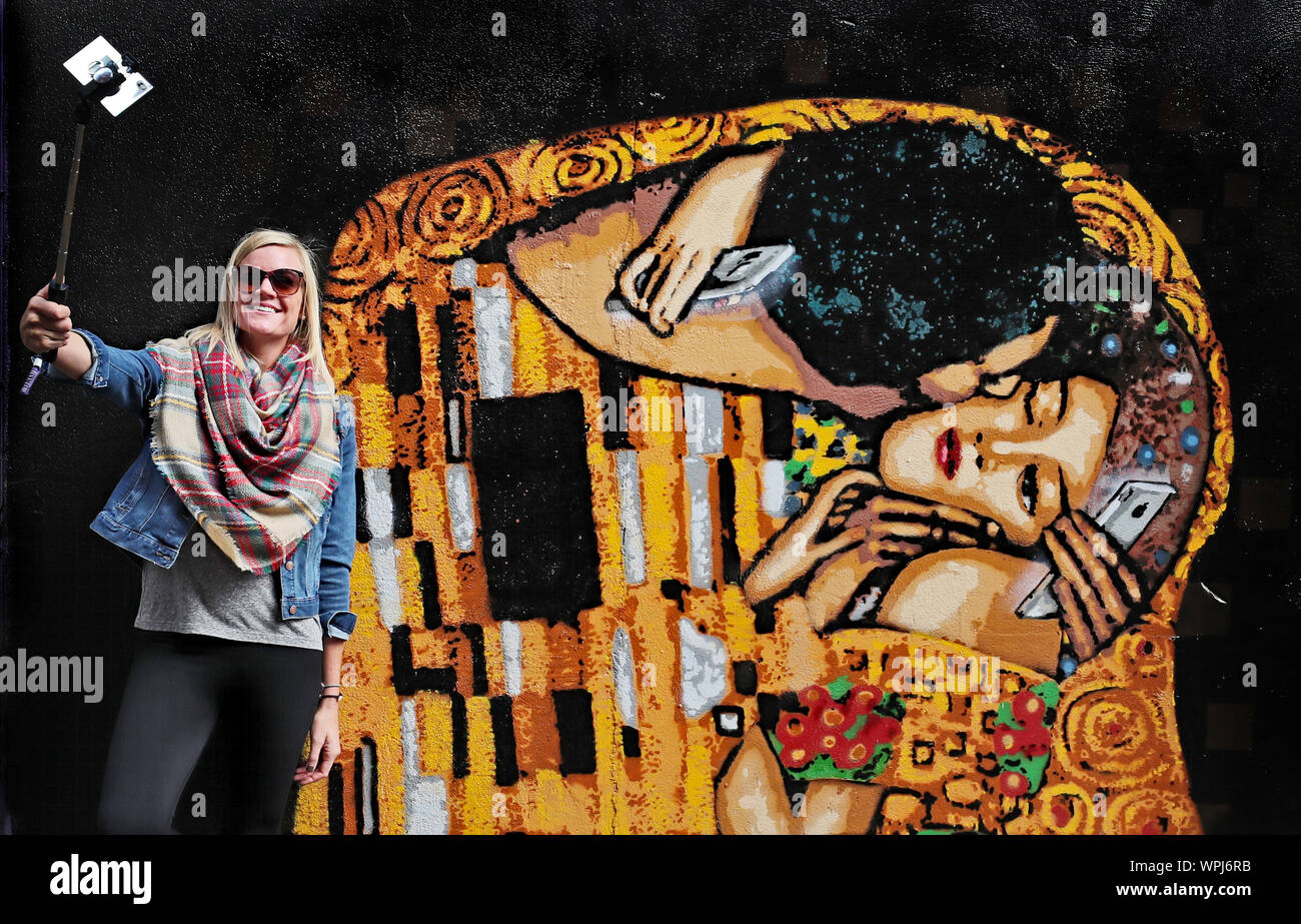 Un turista prende una foto di arte di strada da Irish stencil ADW artista nel centro della città di Dublino. L'immagine basata su Il Bacio di Gustav Klimt, mette in luce la piaga del telefono cellulare dipendenza. Foto Stock