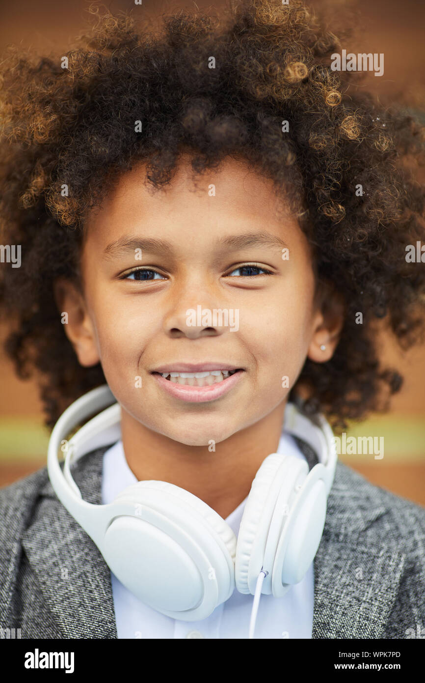 Ritratto di Allegro ragazzo africano con i capelli ricci e con le cuffie intorno al suo collo sorridente in telecamera Foto Stock