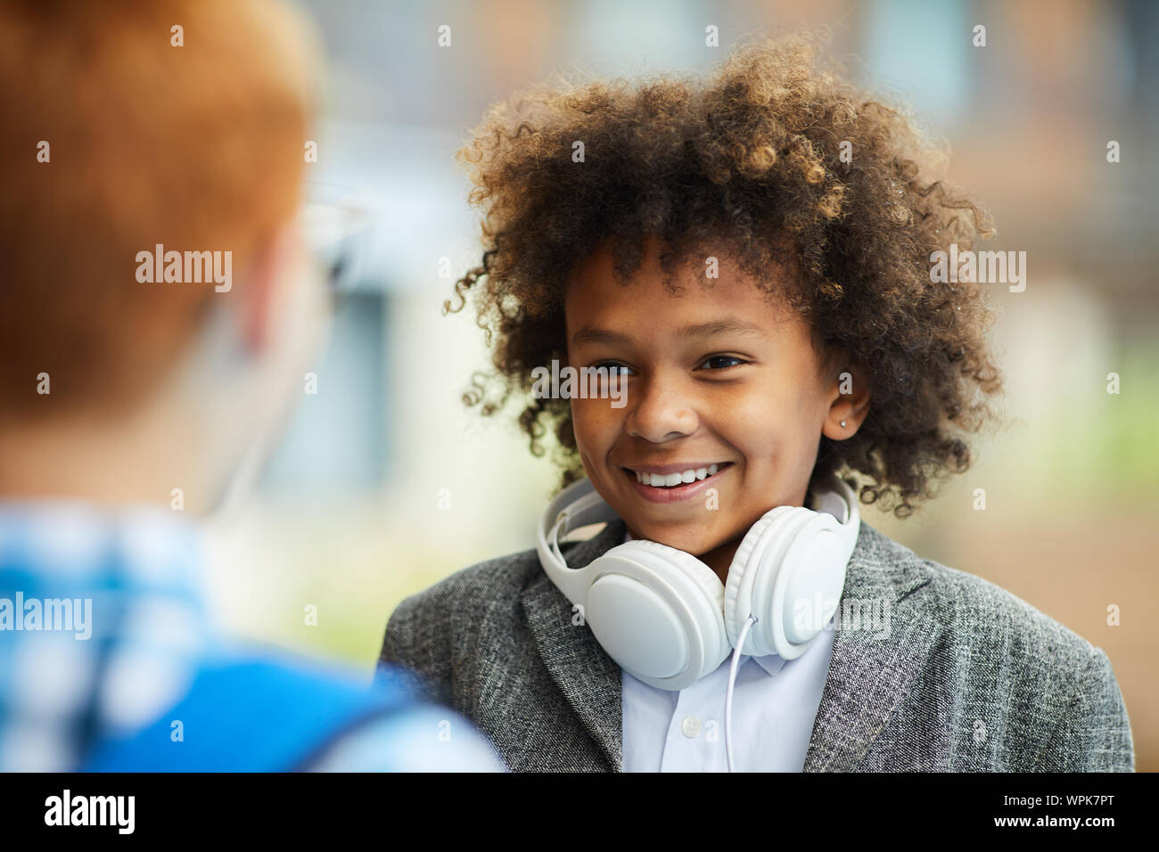 Ragazzo africano con i capelli ricci e con le cuffie a sorridere al suo amico mentre si parla con lui all'aperto Foto Stock
