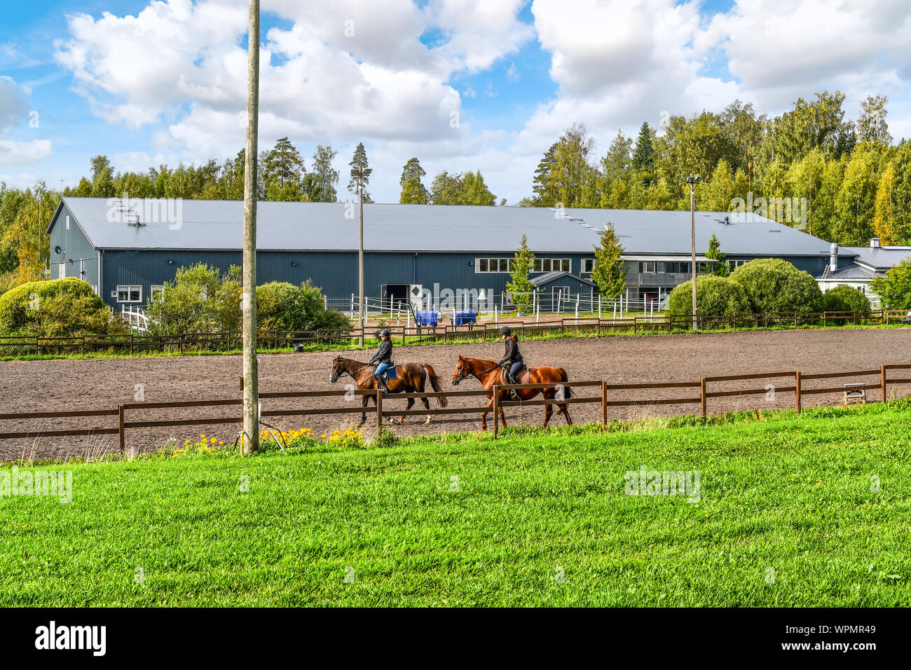 Due femmina equestrians cavalcare cavalli purosangue in un allevamento di cavalli di fronte un grande cavallo indoor arena presso la città di Sipoo Finlandia Foto Stock