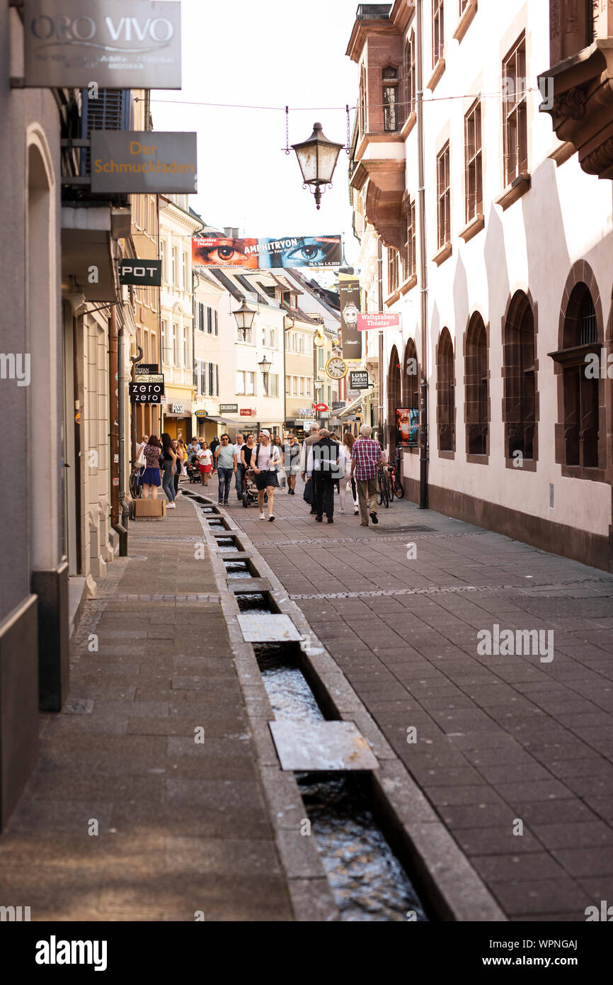 Negozi e una delle famose piste di acqua dolce costeggiano la strada di Rathausgasse, nel centro storico di Friburgo in Breisgau, Germania. Foto Stock