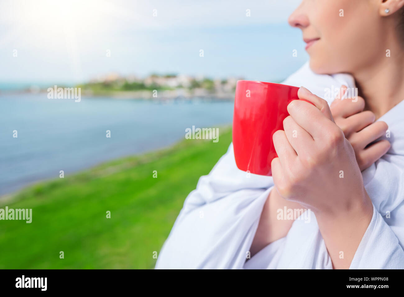 Ragazza avvolto in un lenzuolo sul balcone al mattino beve caffè o tè. Foto Stock