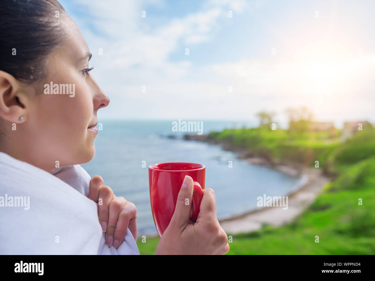 Ragazza avvolto in un lenzuolo sul balcone al mattino beve caffè o tè. Foto Stock