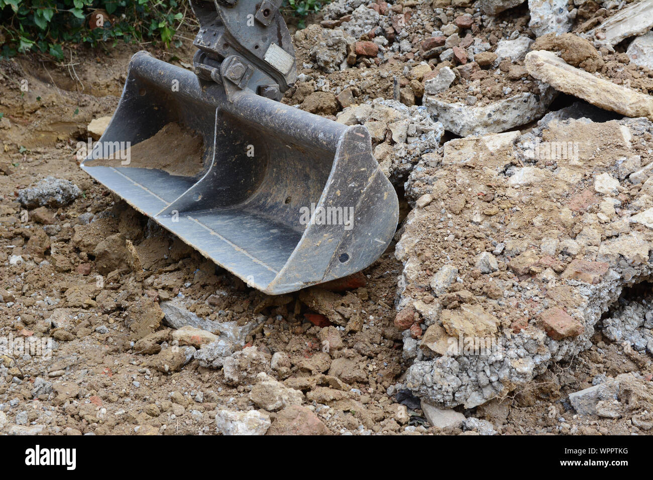In metallo per impieghi pesanti della benna di scavo tra cumuli di terra ruvida e calcestruzzo di pietrisco, scavo di un viale di ingresso Foto Stock