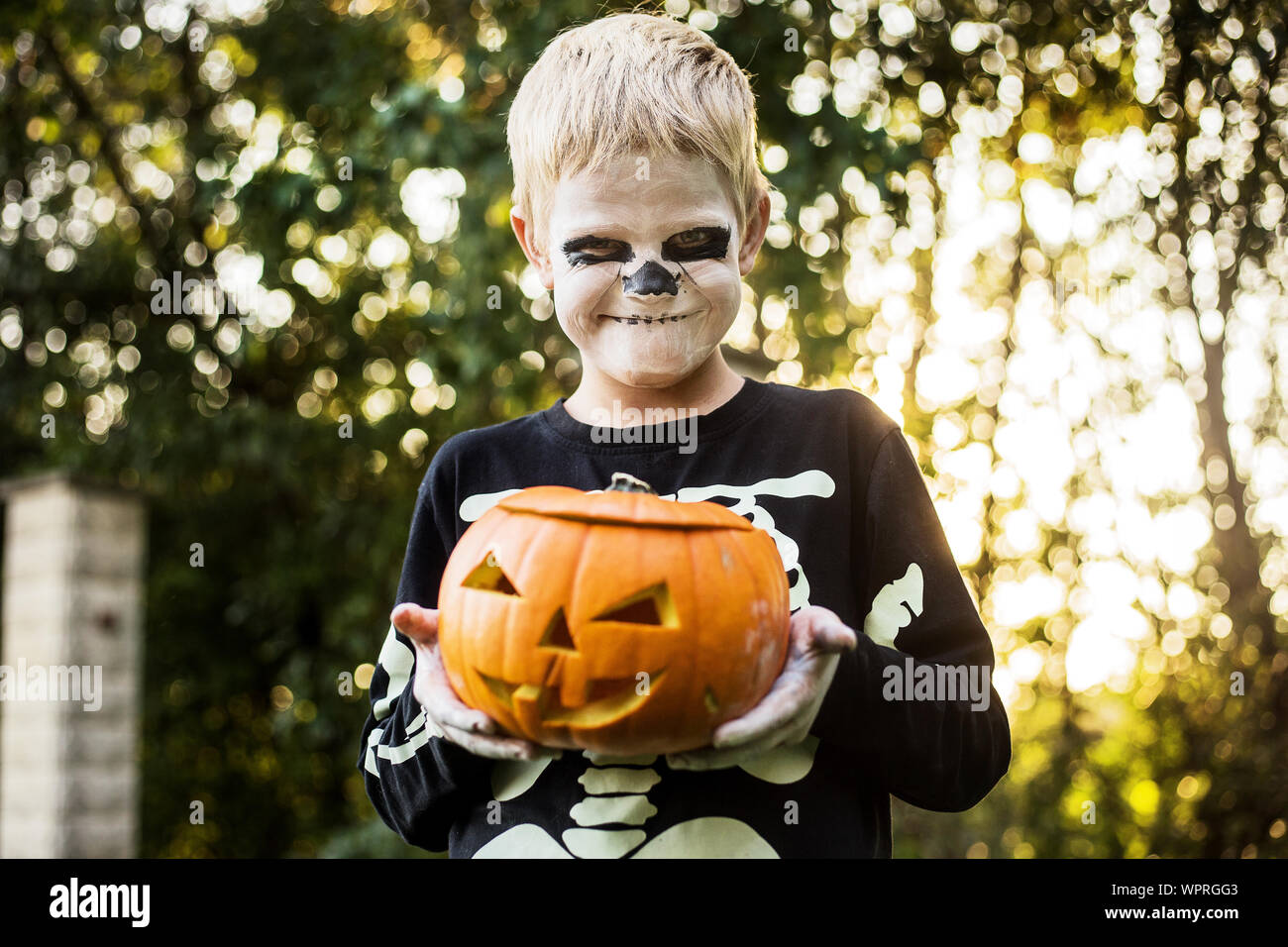 Felice giovani capelli biondi ragazzo con costume scheletro holding jack o lanterna. Halloween. Dolcetto o scherzetto. Ritratto all'aperto Foto Stock