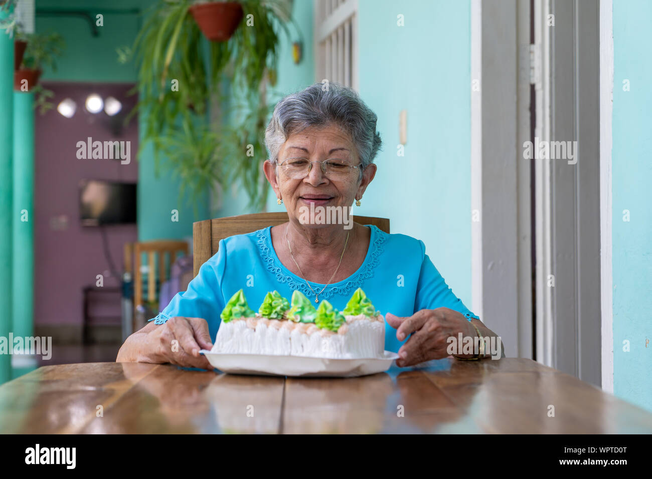 Anziani stropicciata donna seduta e una torta sul tavolo Foto Stock