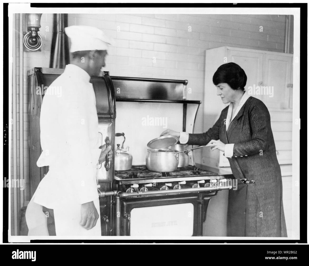 Mary Roberts Rinehart, sollevando il coperchio della pentola sulla stufa, e lo chef in piedi accanto ad Foto Stock