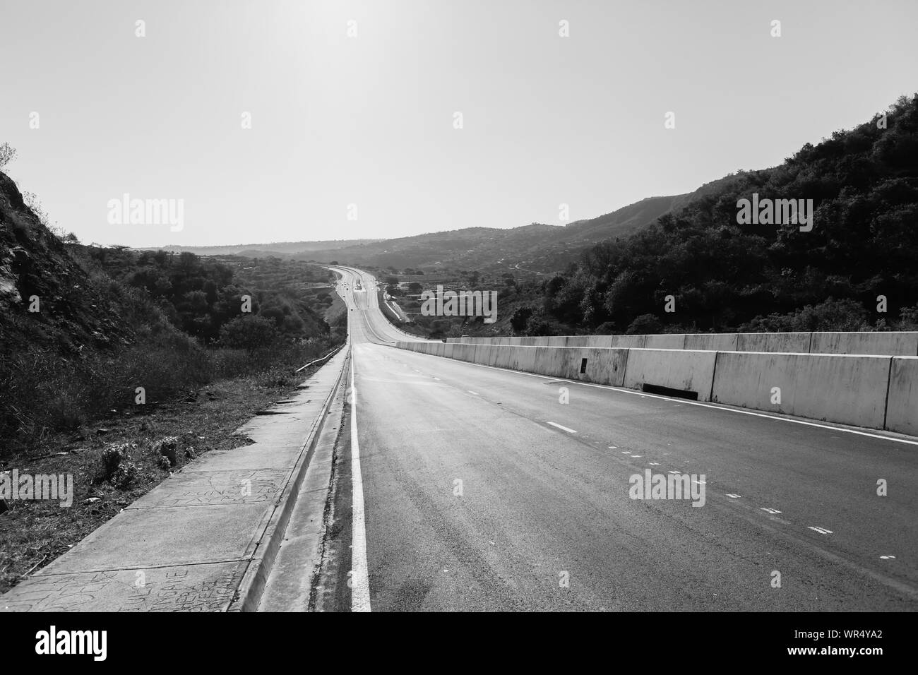 Nuova strada autostrada con pareti in calcestruzzo e la piscina corsie avvolgimento verso il basso attraverso la valle rurale paesaggio vintage bianco nero photo. Foto Stock