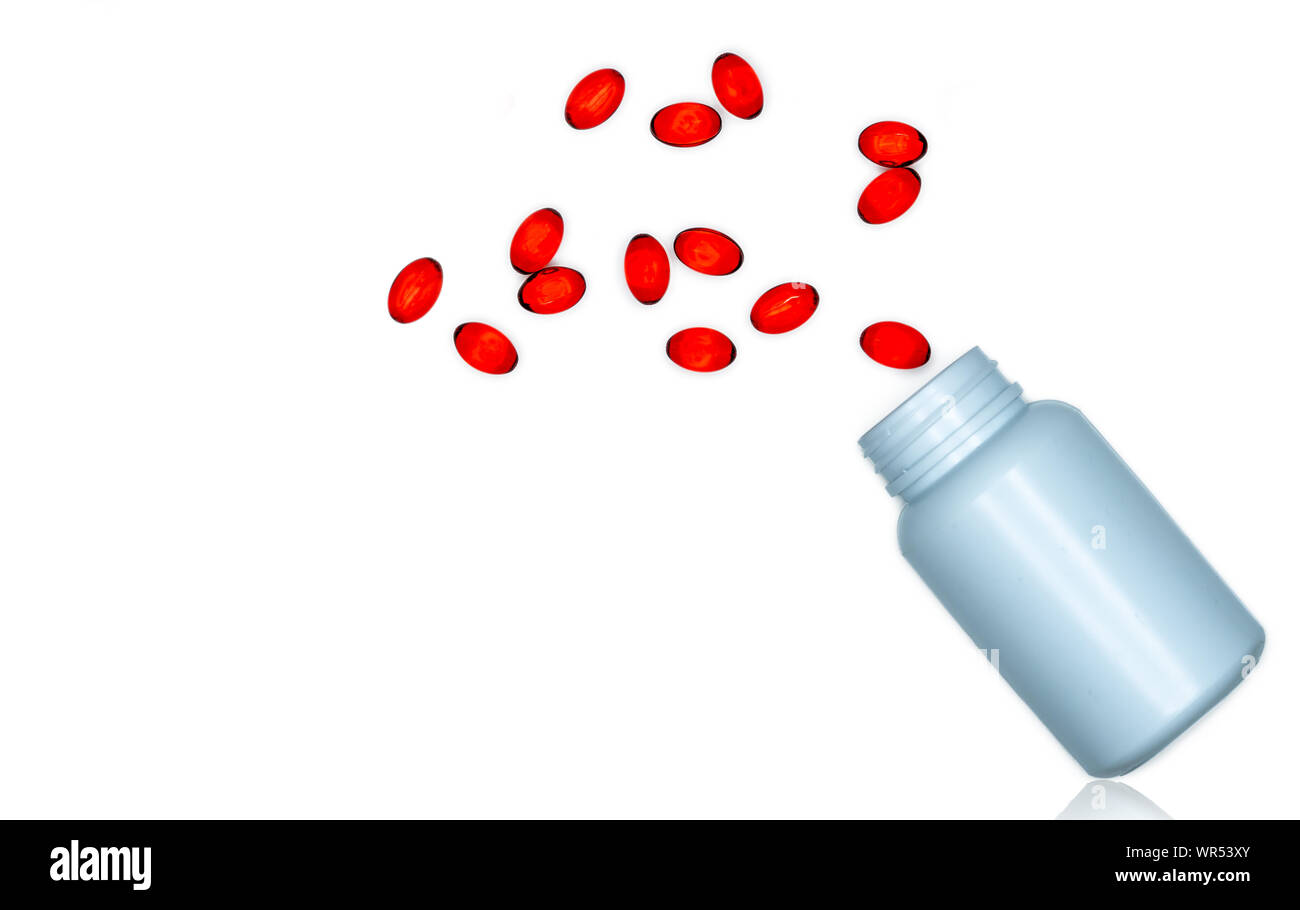 Versare morbido rosso capsula di gel pillole fuori del flacone di farmaco isolati su sfondo bianco. Red capsula di gelatina soffice vitamine e integratori alimentari. Farmacia Foto Stock