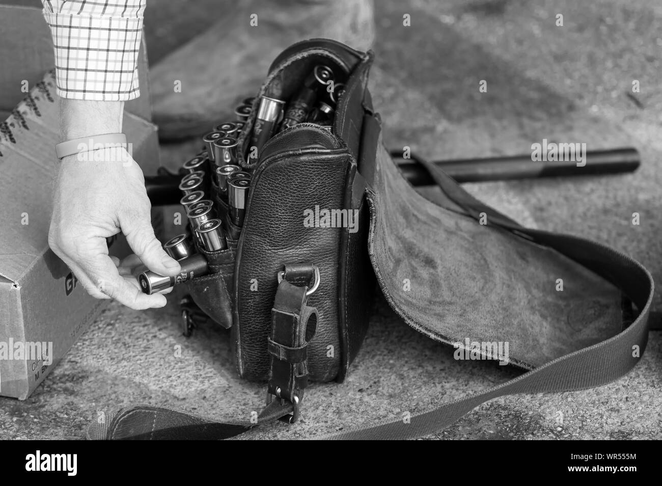 Braccio Mans mostrato picking shotgun cartuccia fuori dalla borsa di pelle sul pavimento (monocromatico) Foto Stock