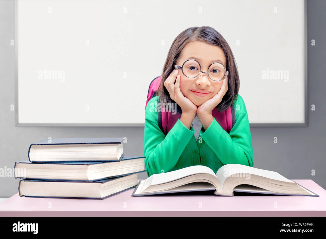 Asiatica ragazza carina con gli occhiali e zainetto seduta e di leggere il libro con sfondo whiteboard Foto Stock