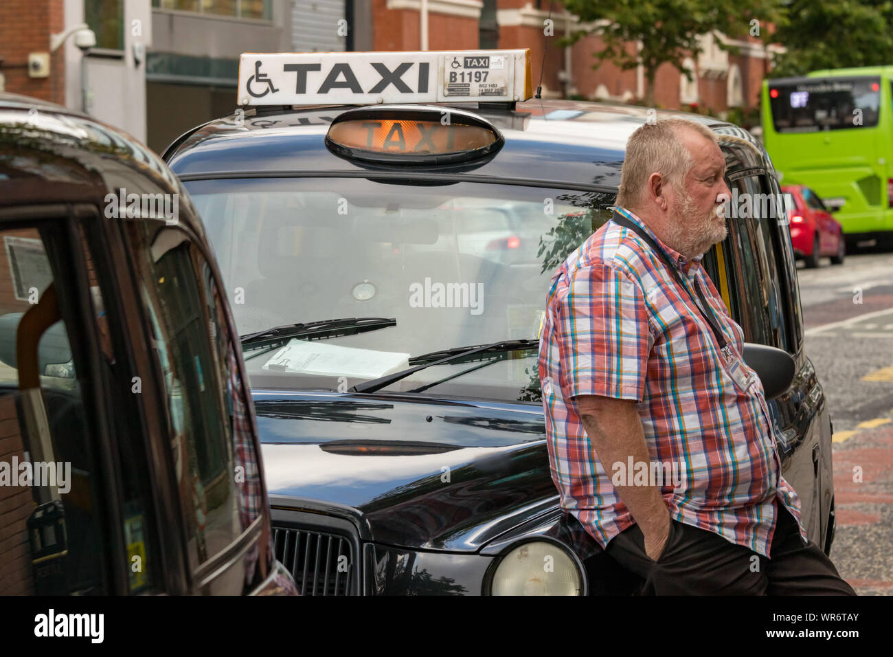 Belfast, Irlanda del Nord, Regno Unito - 31 Luglio 2019: un maschio di taxi driver seduti all'aperto sulla sua vettura in attesa per i clienti a Belfast, Irlanda del Nord, Regno Unito. Foto Stock