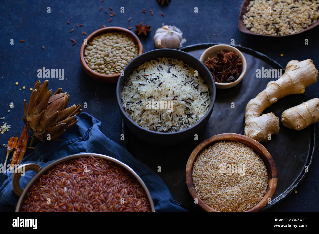 I vari tipi di riso e cereali con spezie su sfondo blu. Riso marrone e mescolate il riso selvatico. Foto Stock