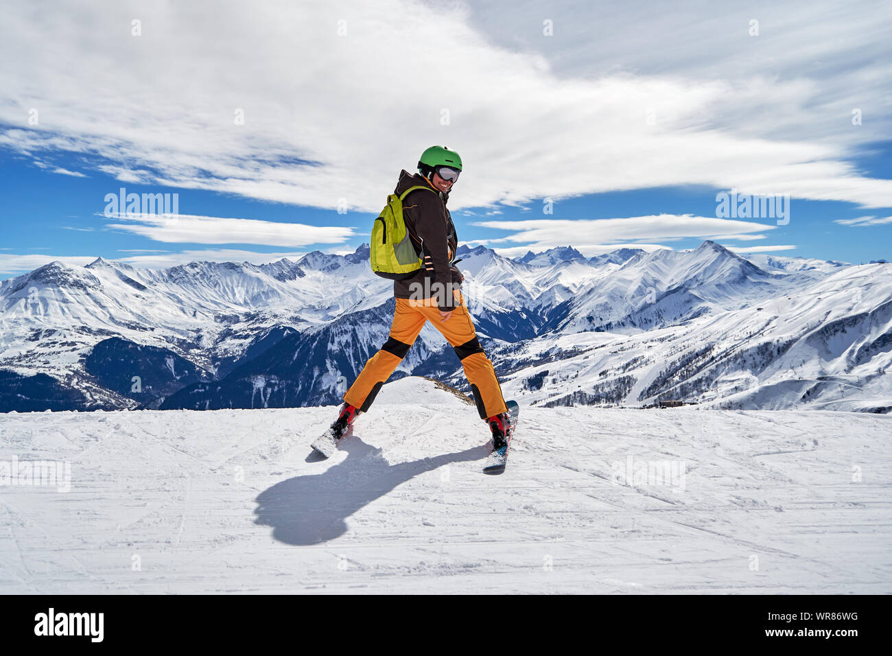 Sciatore uomo sorridente e posa con un bellissimo inverno panorama di montagna in Les Sybelles ski domain, Francia, in una giornata di sole con cielo azzurro e bianco clou Foto Stock