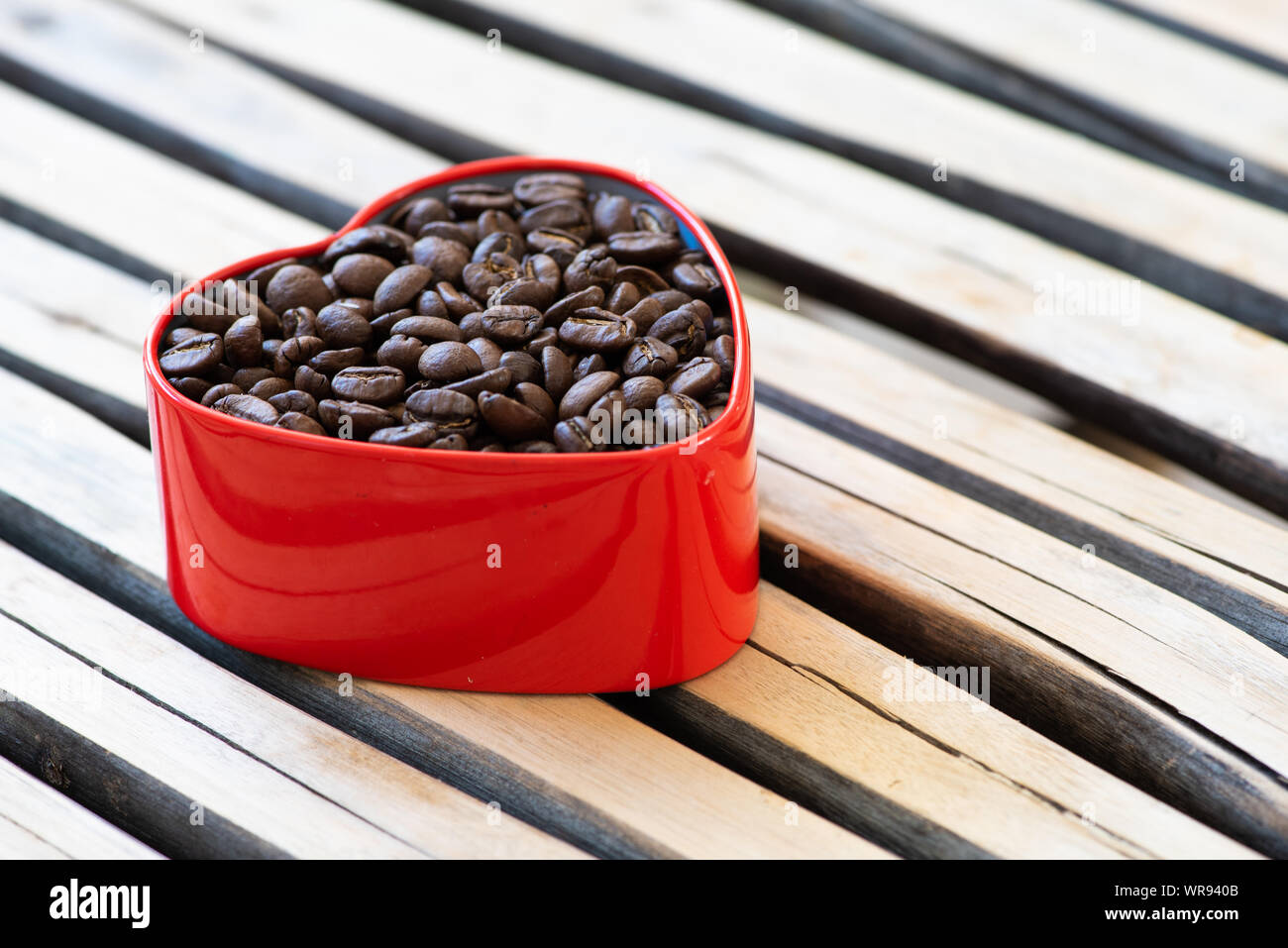 I chicchi di caffè in un cuore-stagno sagomati disposti su un sfondo di legno. Foto Stock