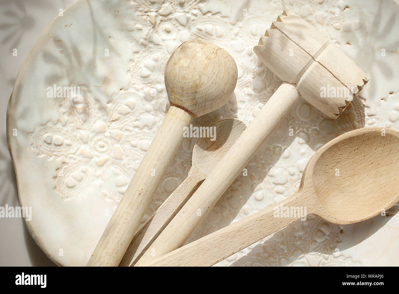 Accessori per la cucina. Cucchiaio di legno, stick e un pestello di carne su una ceramica lastra decorata. Foto Stock