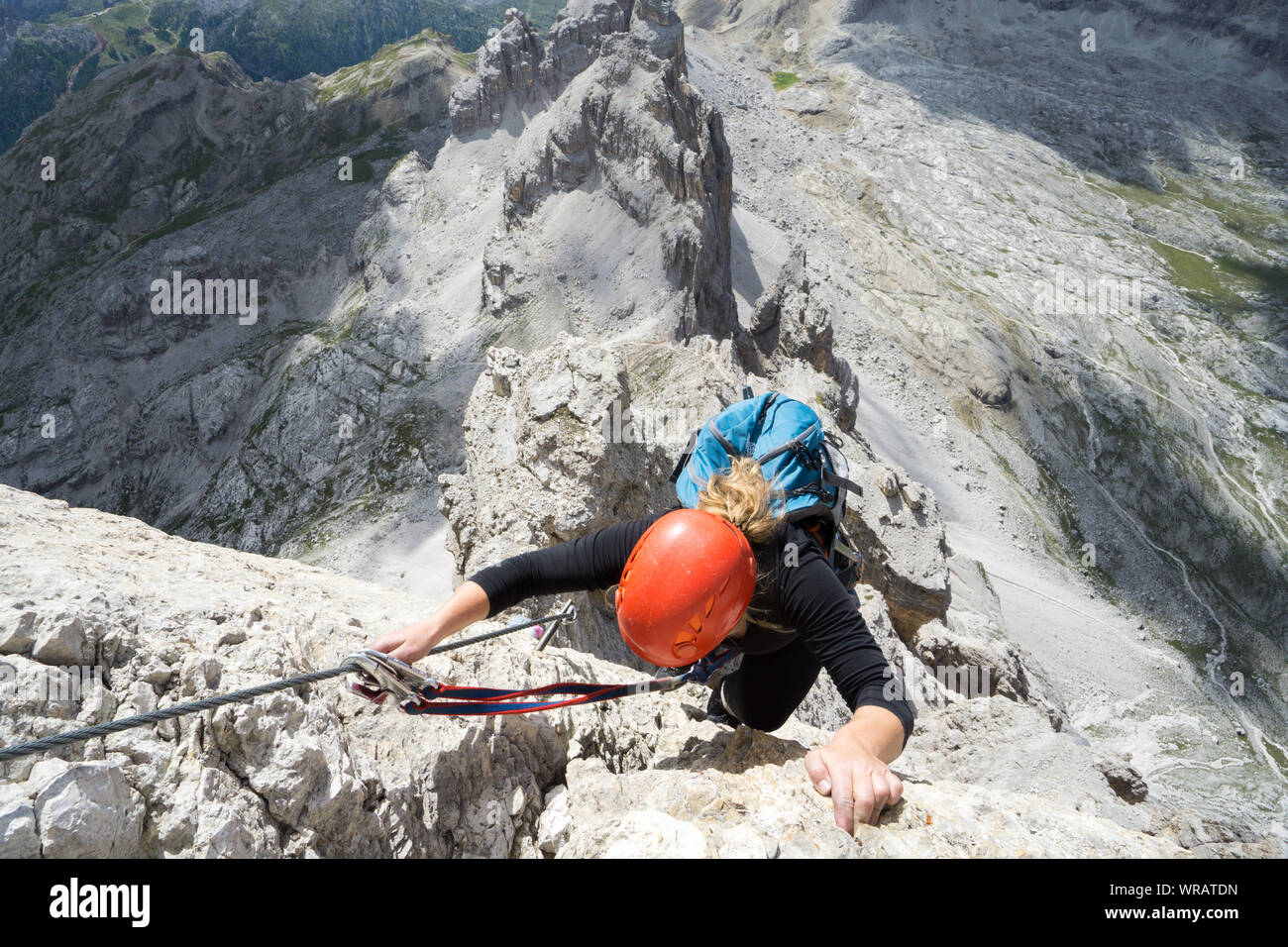Vista orizzontale di un attraente bionda alpinista femmina su una ripida Via Ferrata delle Dolomiti italiane con una grande vista dietro Foto Stock