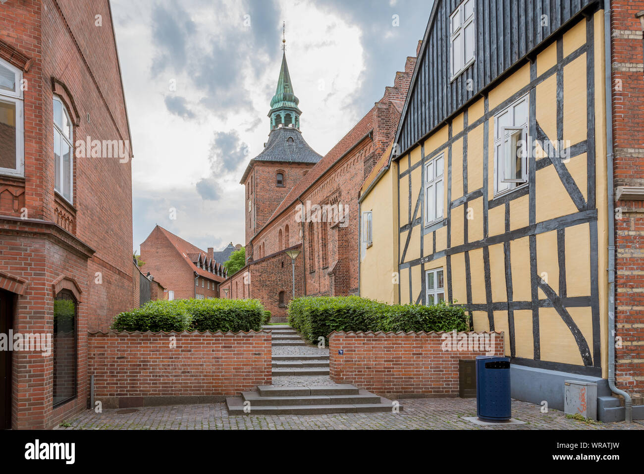 Un antico giallo casa in legno e muratura con la chiesa in background nei vecchi quartieri di Svendborg, Danimarca, luglio 10, 2019 Foto Stock
