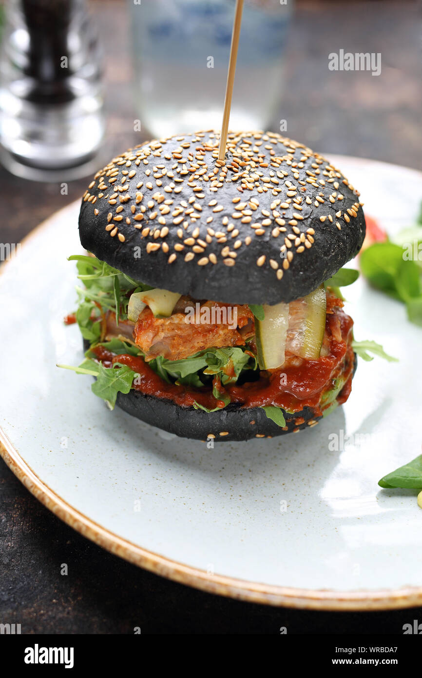 Burger in una black bun con carne tritata, cetriolo sottaceto e ketchup servita su una piastra. Foto Stock