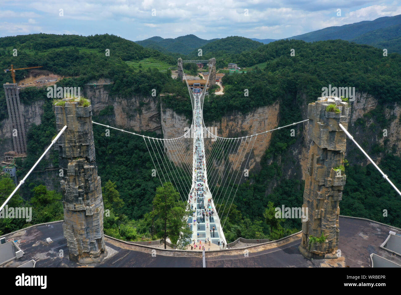 In questa vista aerea, turisti brave la più lunga del mondo e il più alto dal fondo di vetro ponte sopra il Zhangjiajie Grand Canyon a Wulingyuan Scenic e H Foto Stock