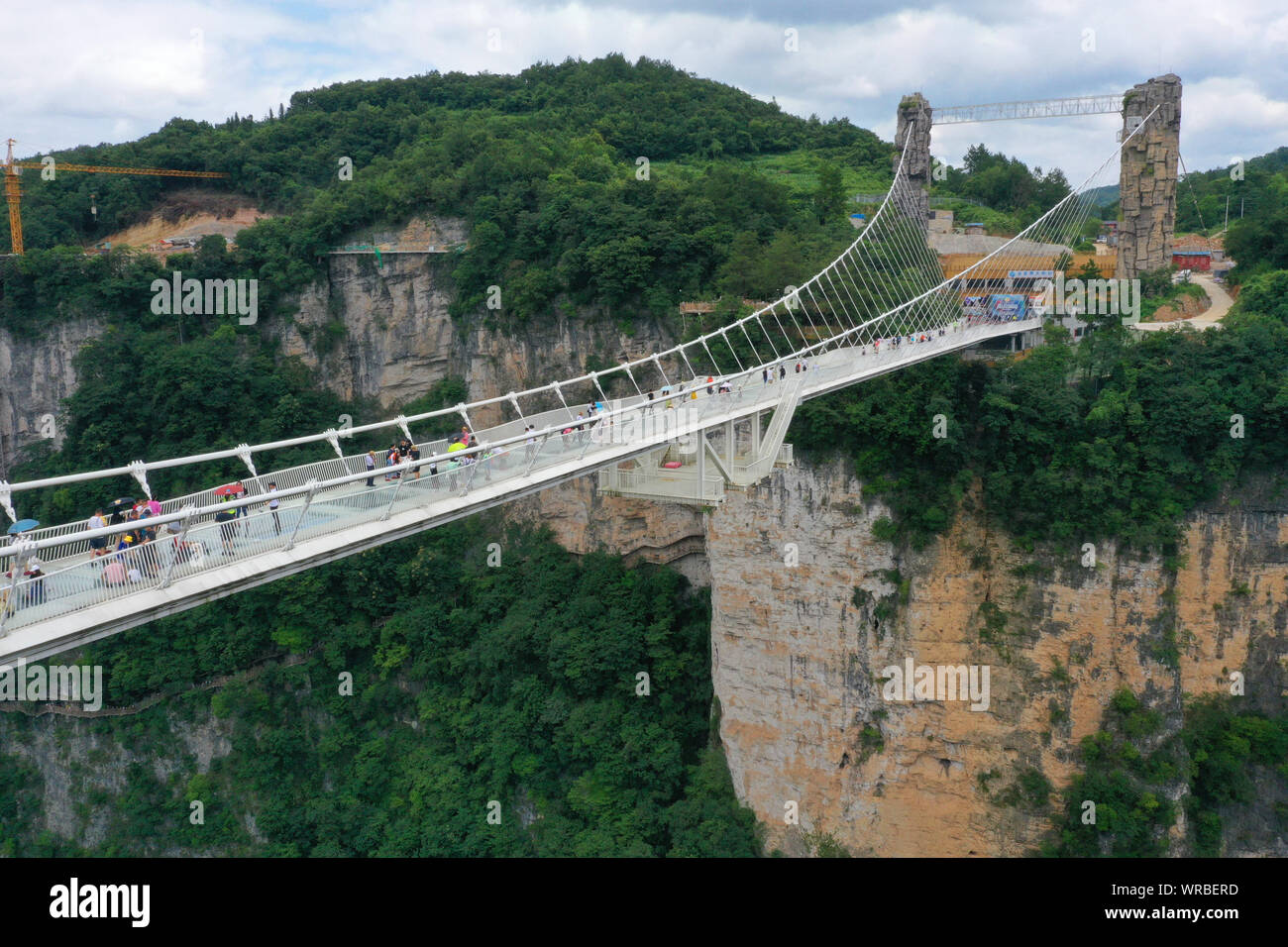 In questa vista aerea, turisti brave la più lunga del mondo e il più alto dal fondo di vetro ponte sopra il Zhangjiajie Grand Canyon a Wulingyuan Scenic e H Foto Stock