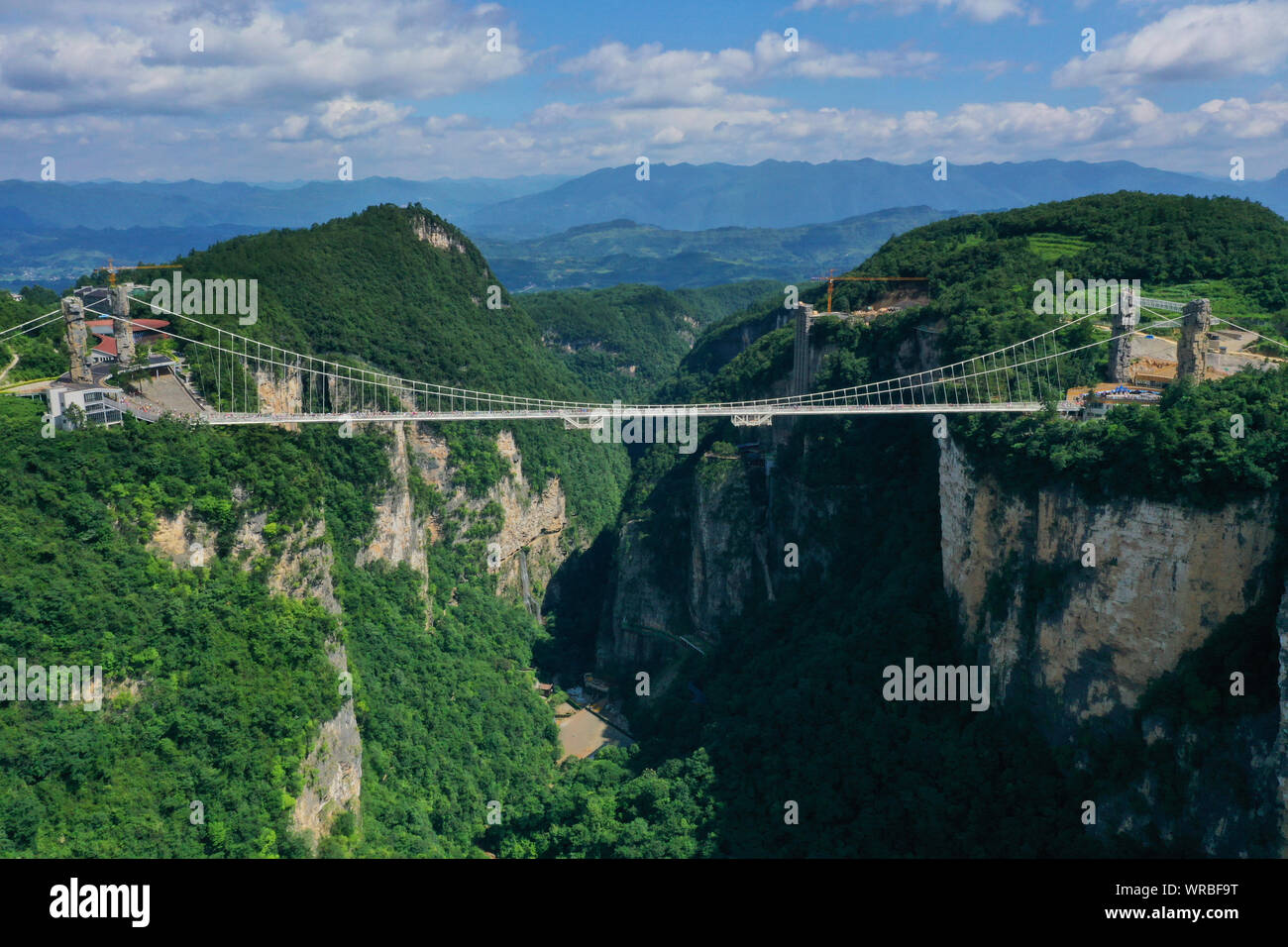 In questa vista aerea, turisti brave la più lunga del mondo e il più alto dal fondo di vetro ponte sopra il Zhangjiajie Grand Canyon a Wulingyuan Scenic e H Foto Stock