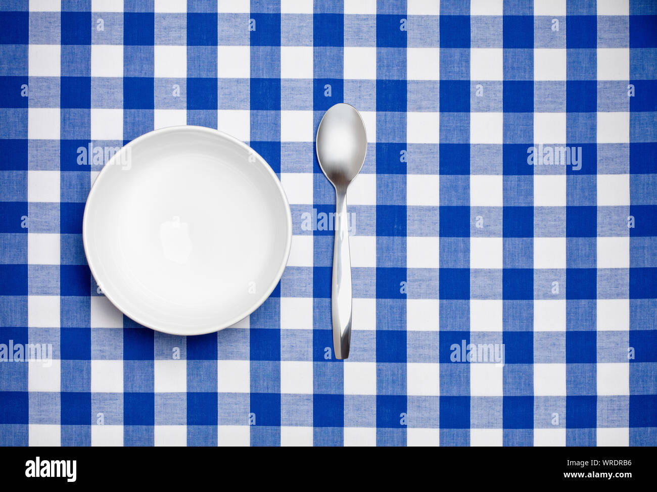 Bianco vuoto ciotola e cucchiaio su un blu tovaglia gingham Foto Stock