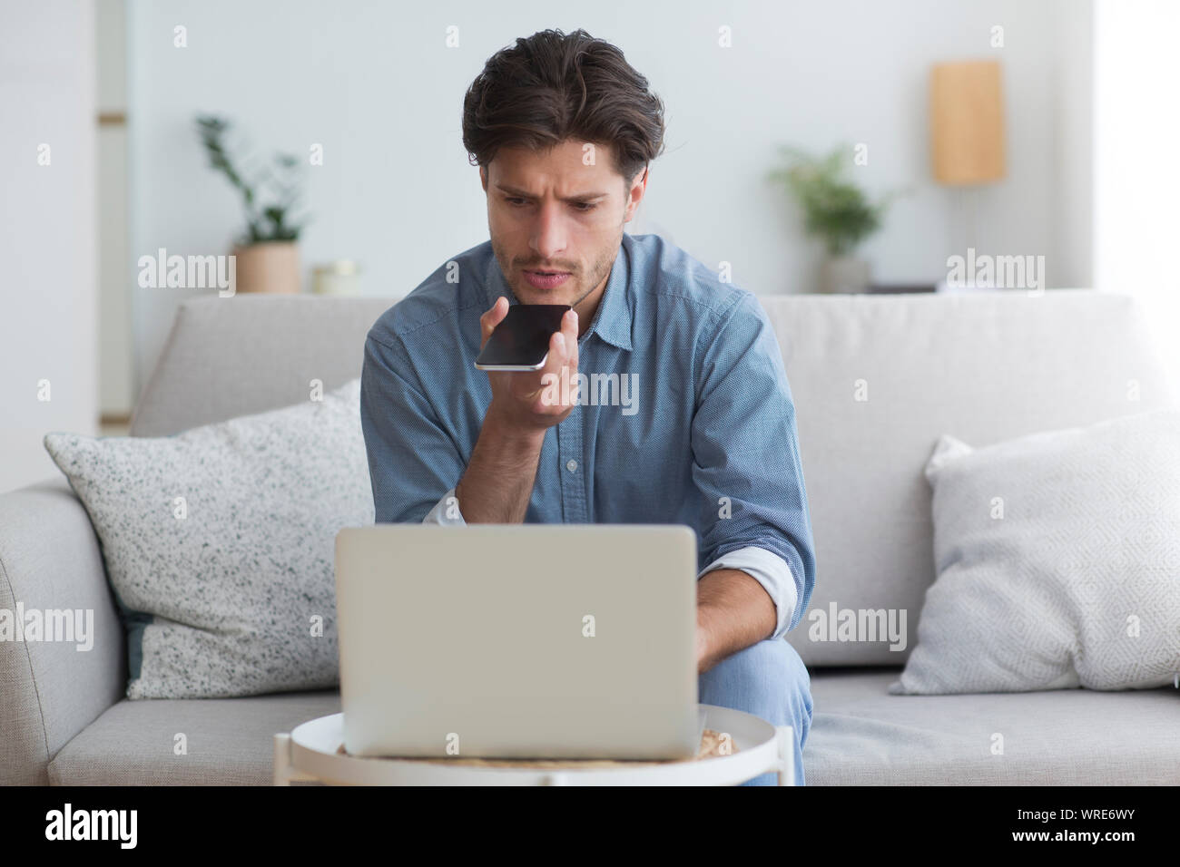 Uomo serio tramite telefono Assistente vocale seduti al computer portatile Indoor Foto Stock