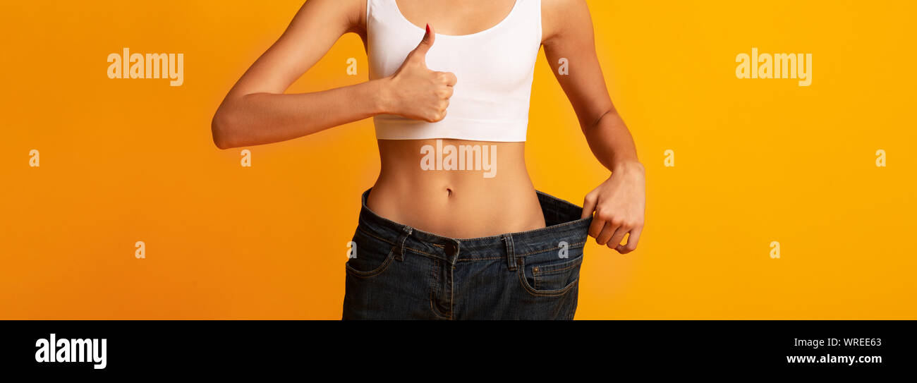 Irriconoscibile giovane donna in pantaloni Oversize gesticolando Thumbs-Up, Studio Shot Foto Stock