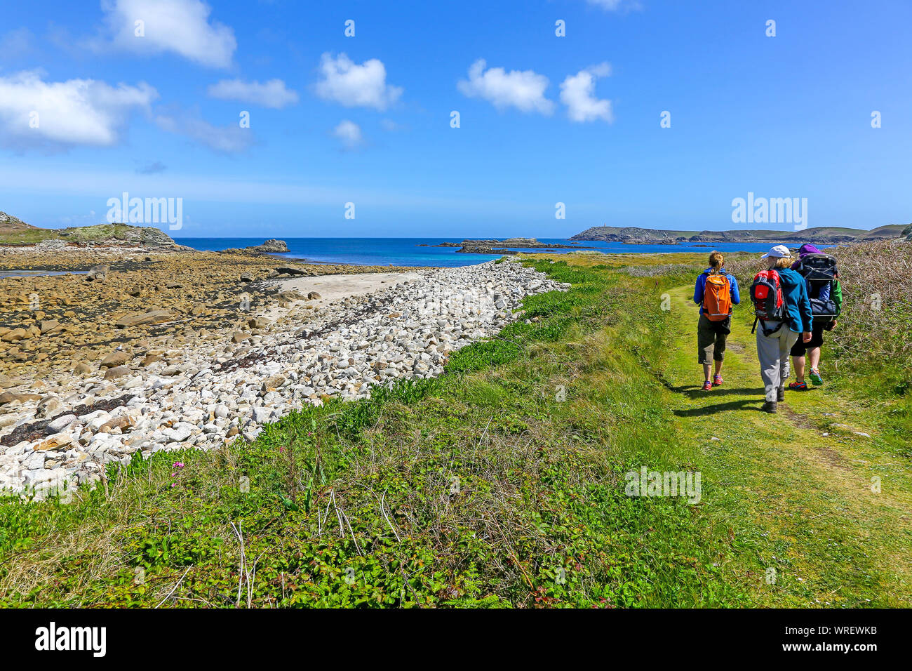 3 persone che camminano verso la grande baia e la segnalazione su San Martin's Island, isole Scilly, Cornwall, Regno Unito Foto Stock