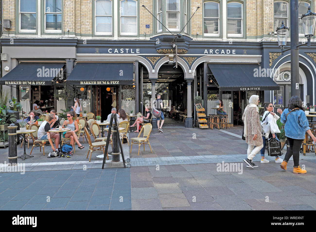 Le donne a piedi nella St Mary Street al di fuori del castello Arcade & persone sedute a tavoli fuori Barker Rum & Fizz centro di Cardiff Wales UK KATHY DEWITT Foto Stock