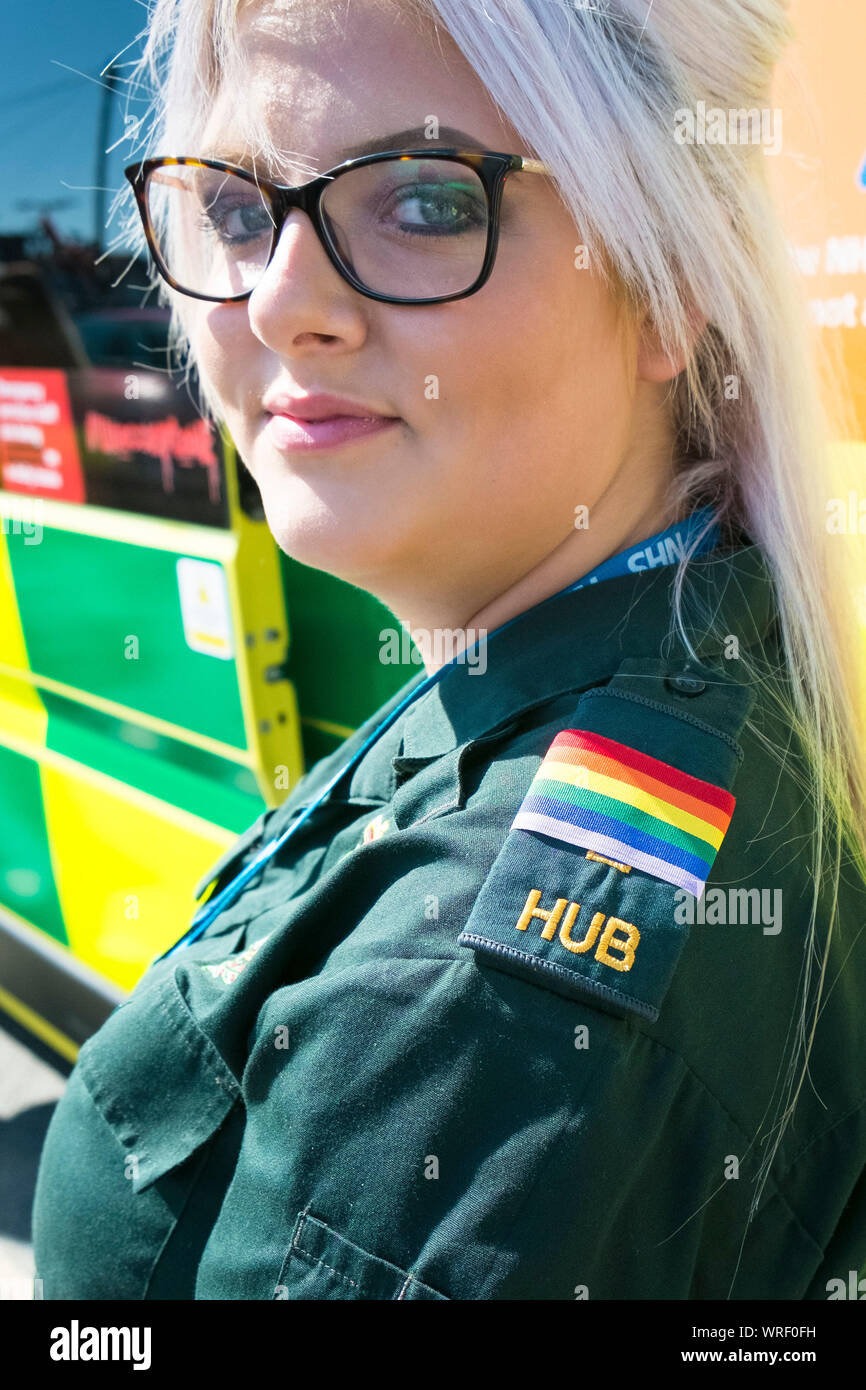 Un ambulanza NHS membro di equipaggio che indossa il Gay Pride epaulettes in piedi di fronte a un'ambulanza al Cornwall Gay Pride Parade di Newquay centro città. Foto Stock