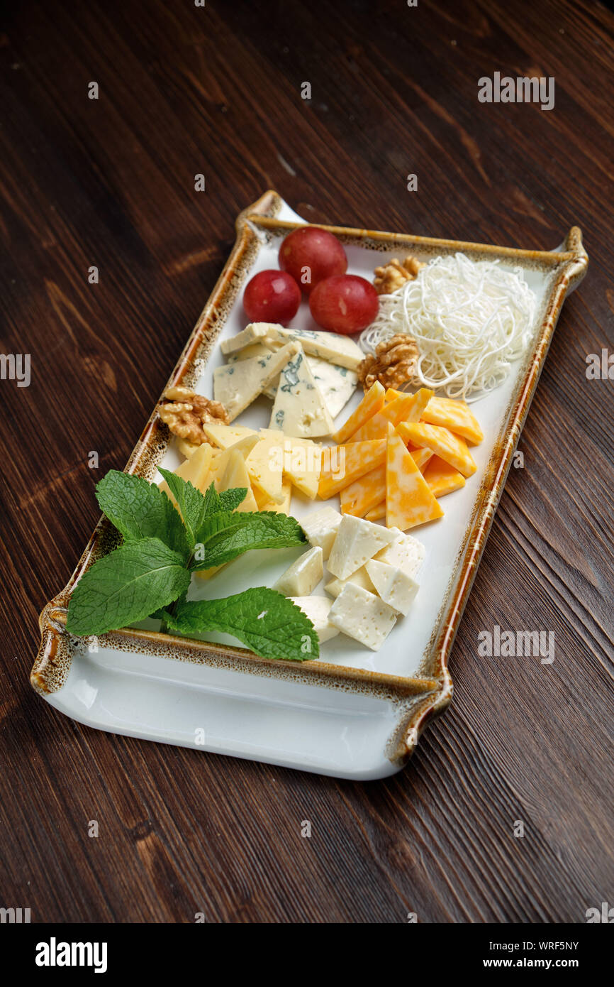 Bella impostazione tabella piatto di formaggio su una piastra bianca su sfondo scuro. Cibo per lo styling. Il menu del ristorante Foto Stock
