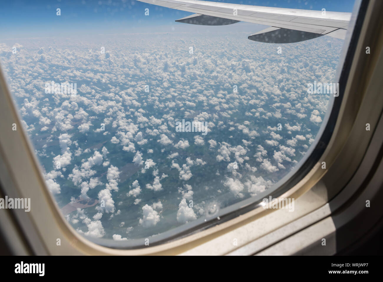 Qui è vista dal piano di oblò sul piano dell'ala, il terreno sottostante e le nuvole di un giorno di estate in volo. Aeroplano, viaggi, jet volo, c Foto Stock