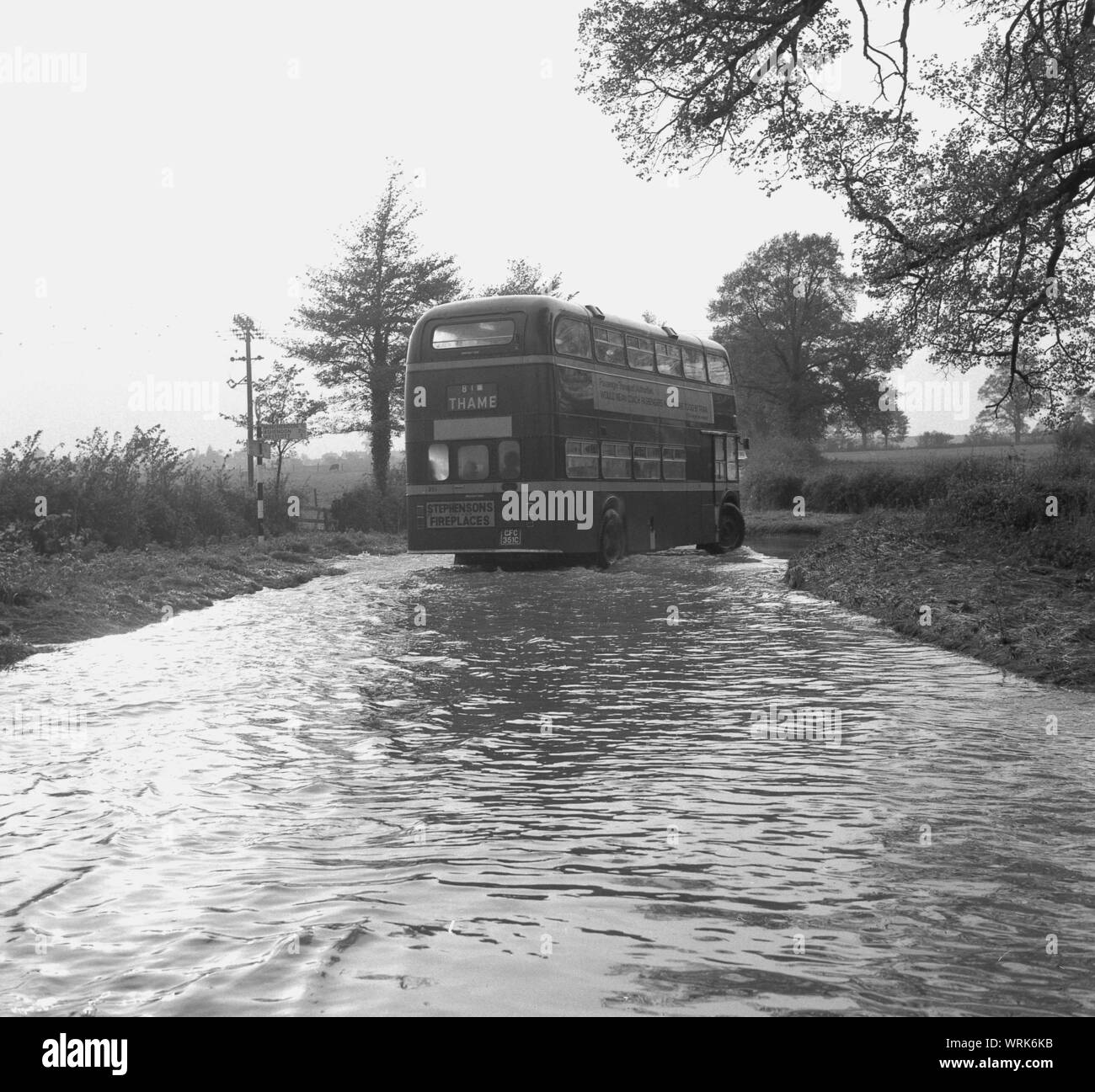 1967, storico, una strada allagata, un double-decker bus diretto a Thame, Bucks, passando attraverso una grande piscina di acqua sulla strada di un paese dove gli scarichi hanno traboccato. Foto Stock