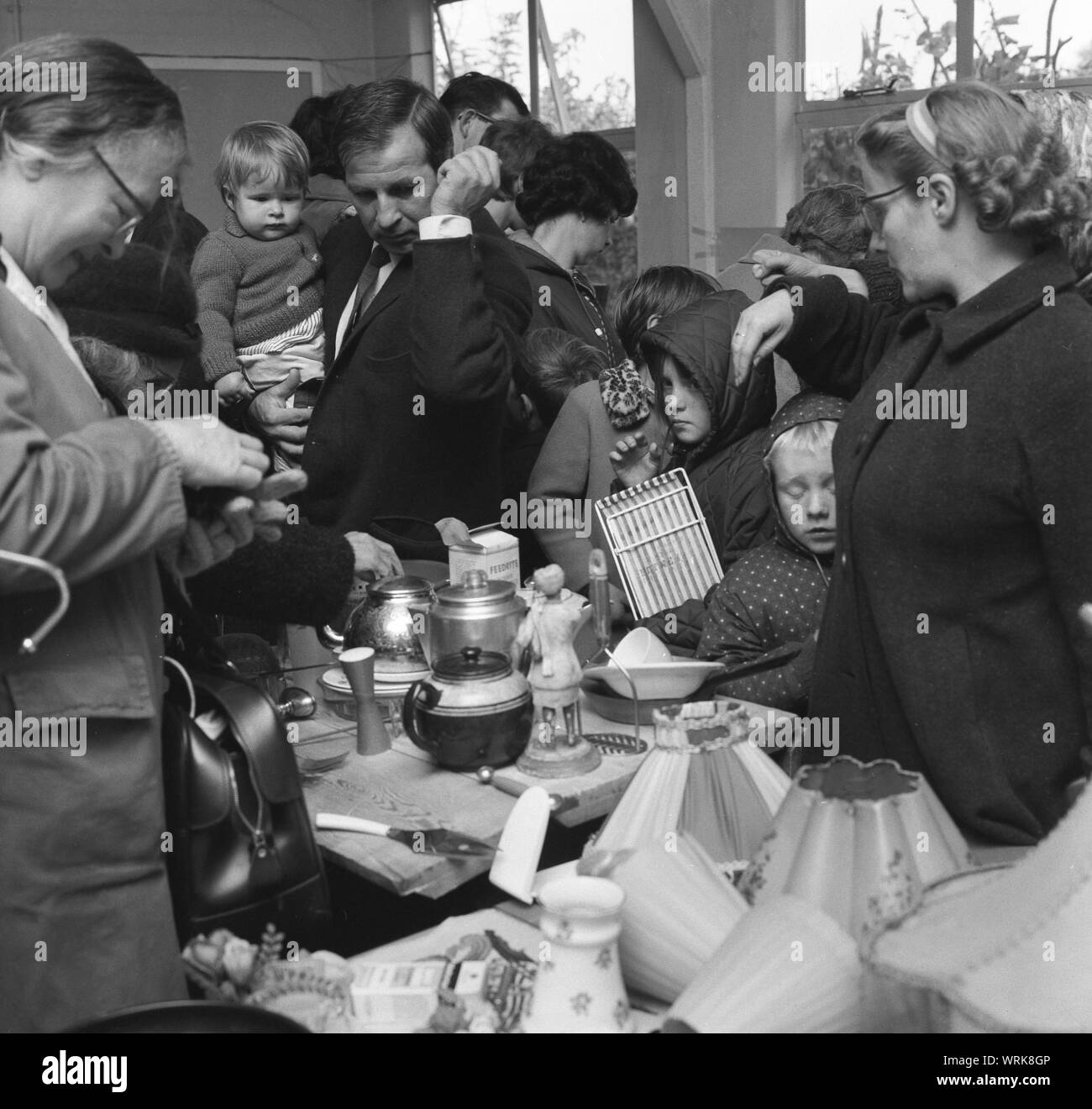 1967, storico, persone all'interno di una camera presso una scuola fundraising accozzaglia di vendita o bazaar, guardando la seconda mano articoli disponibili su uno stallo, Inghilterra, Regno Unito. Foto Stock