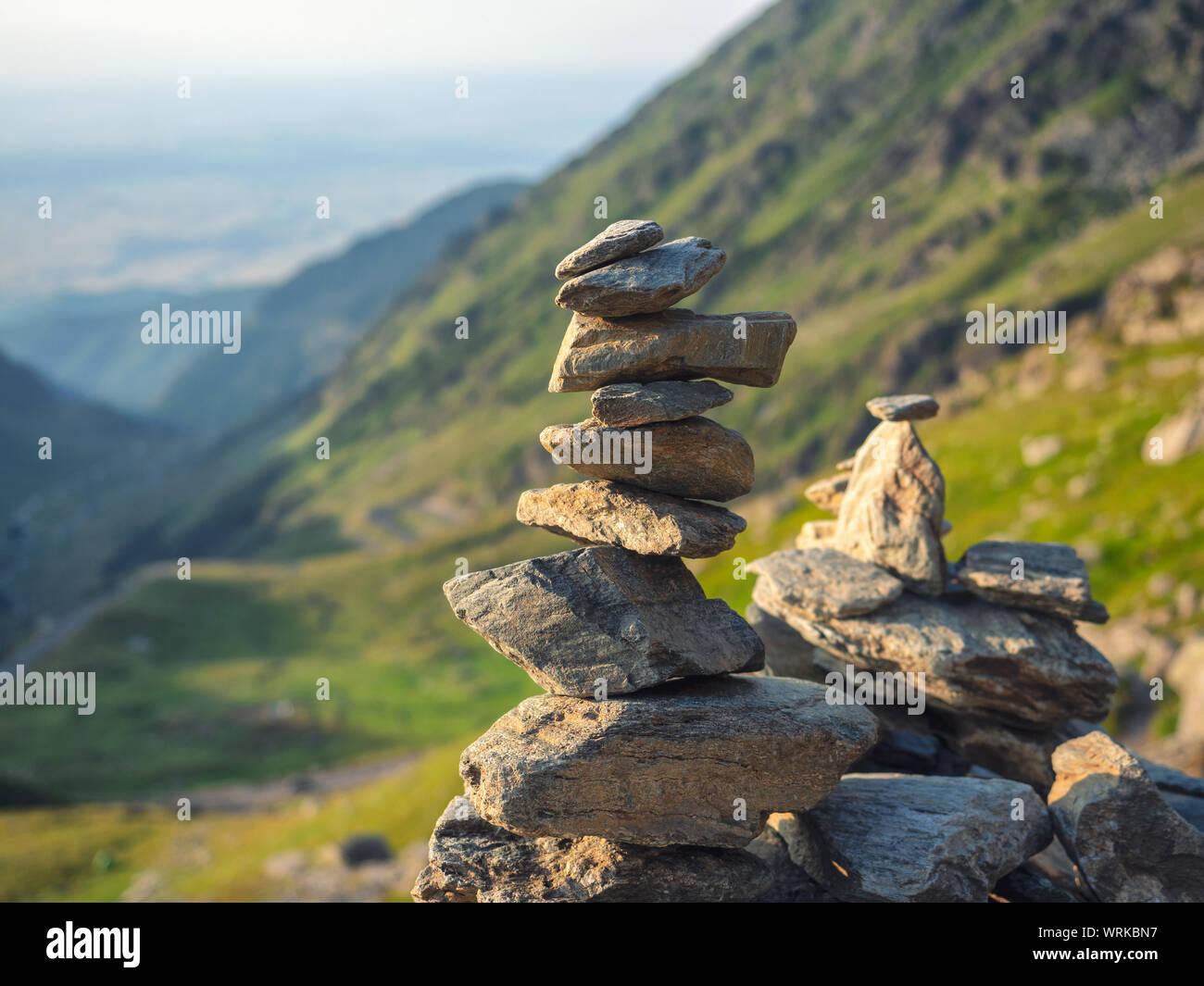 Pila di pietra con pietre equilibrato sulla montagna sfocata sfondo nel tramonto luce calda Foto Stock