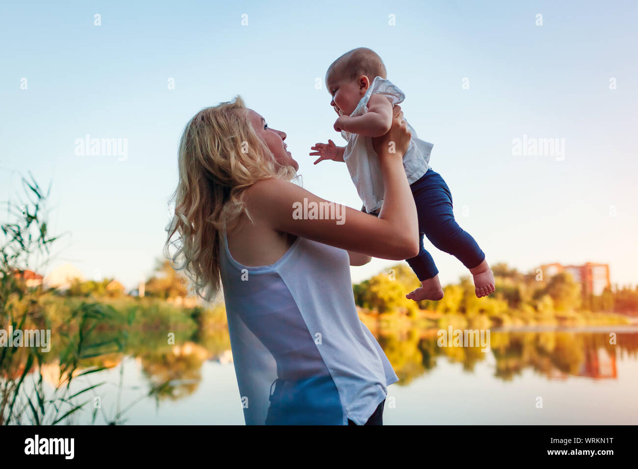 Giovane madre a piedi dal fiume estate con baby girl. La donna il sollevamento di capretto e di divertirsi con il bambino. La famiglia trascorre del tempo insieme Foto Stock