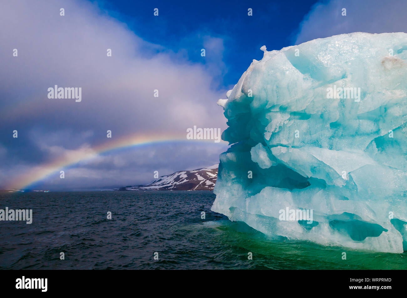 Rainbow stretching per un verde iceberg nell'Oceano Artico, Hornsund Svalbard Norvegia. Foto Stock