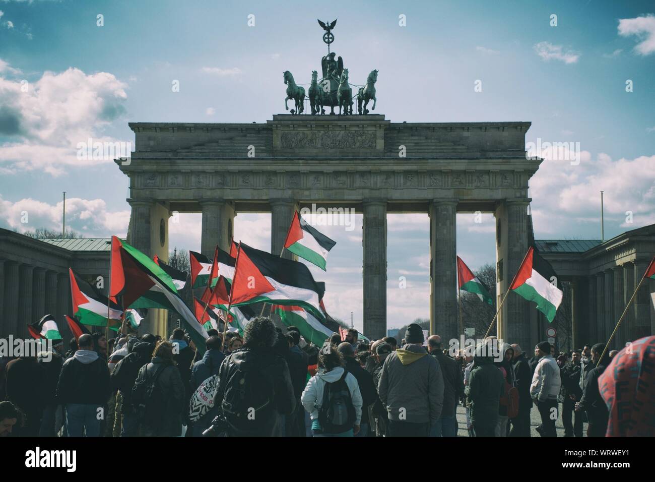 Folla sventolando bandiere palestinese presso la Porta di Brandeburgo contro Sky Foto Stock
