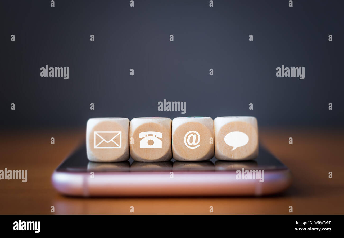 Close-up di un telefono, e-mail, chat e post icone di dadi in legno disponendo in una fila sul telefono cellulare, metodi di contatto. Foto Stock