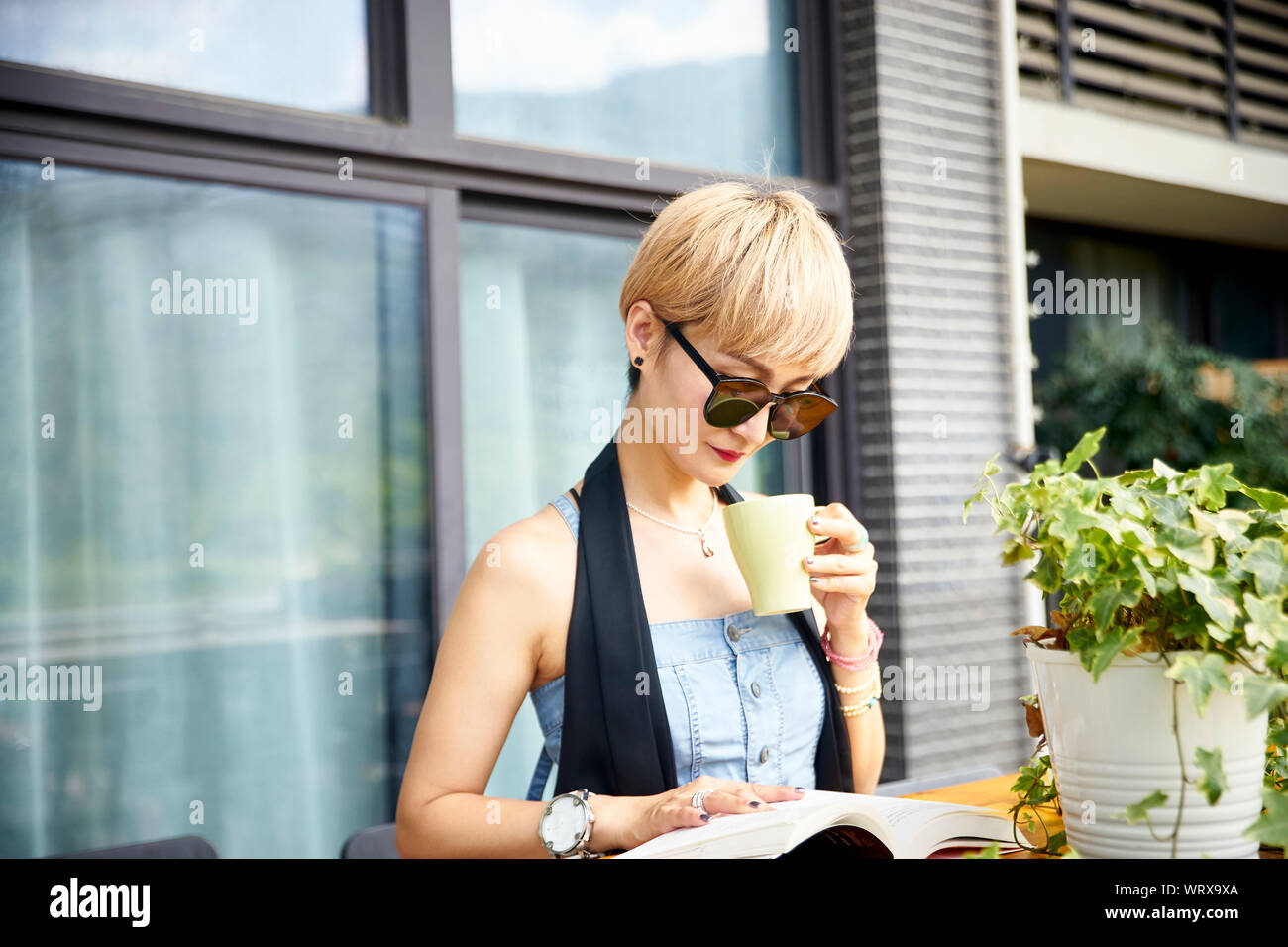 Giovane donna asiatica godendo la lettura e il caffè sul patio Foto Stock