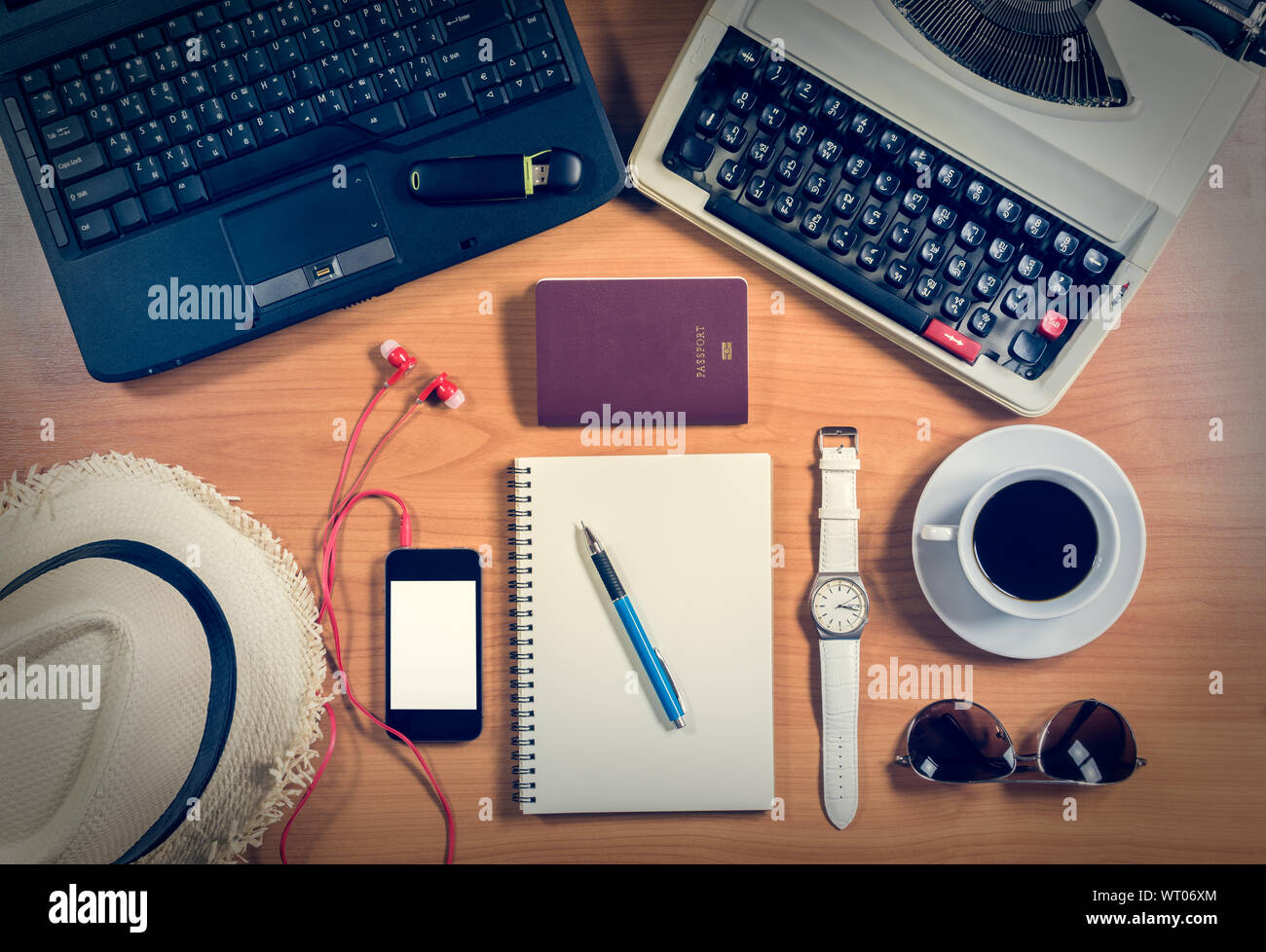 Vista superiore scrivania da ufficio con computer, forniture, tazza di caffè, passaporto, occhiali da sole e cappello e orologio da polso. Foto Stock